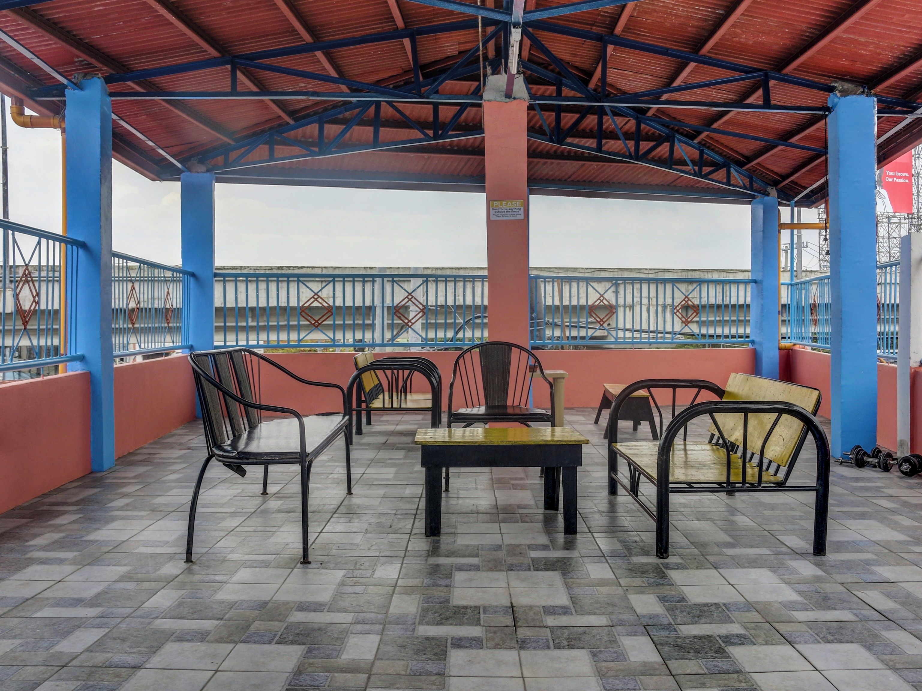 A covered outdoor seating area with tiled flooring, metal chairs, and tables.