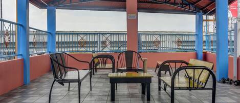 A covered outdoor seating area with tiled flooring, metal chairs, and tables.