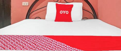 A bed with a white and red patterned bedspread, a red pillow with "OVO" text, and a metal headboard against a pink wall.