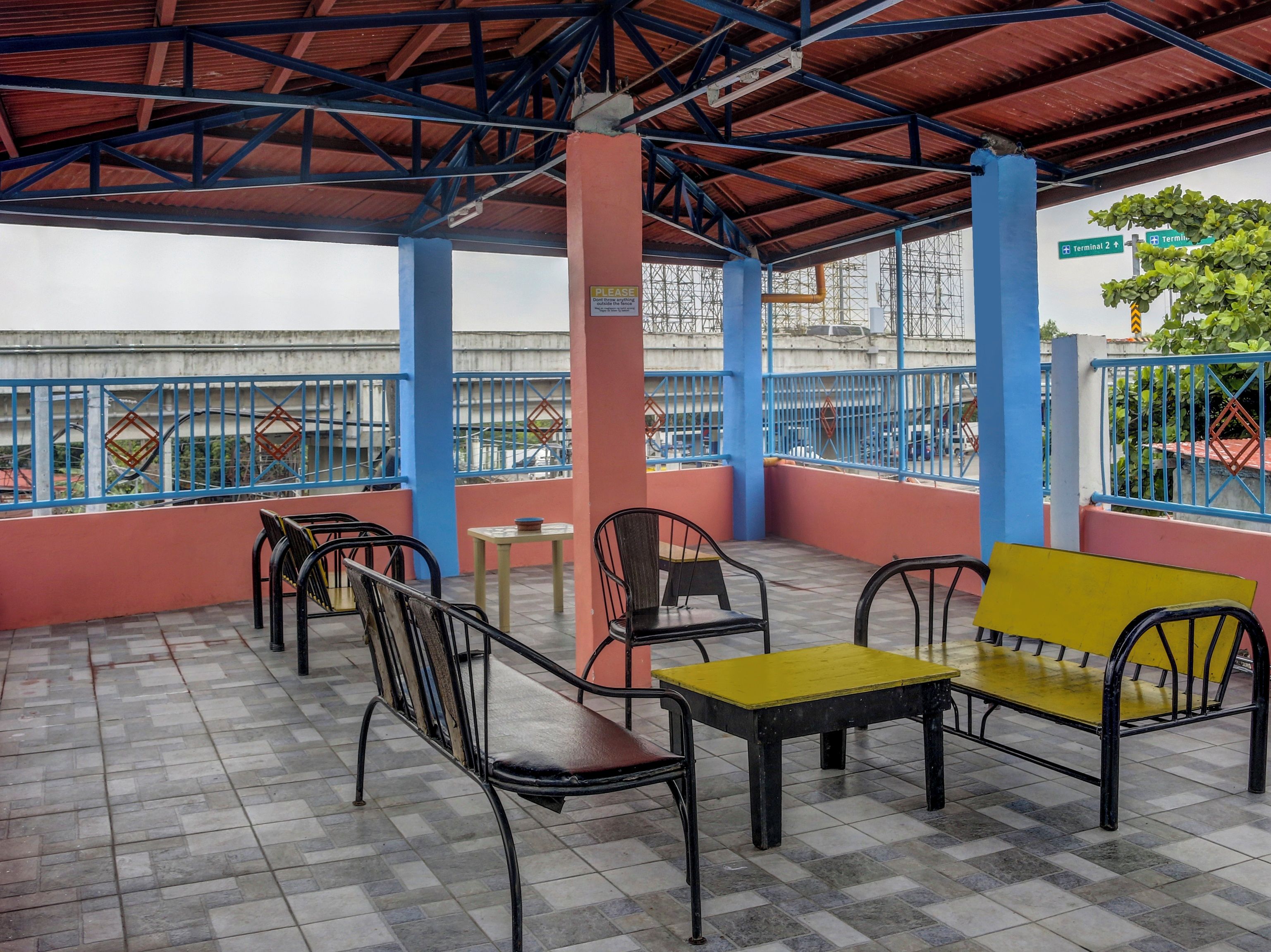 An outdoor seating area with metal chairs and tables, a blue railing, and a view of the cityscape.