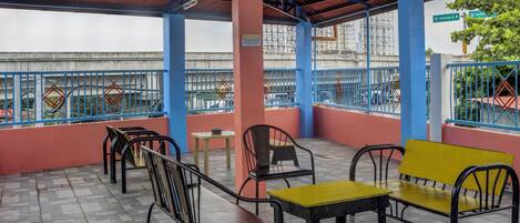 An outdoor seating area with metal chairs and tables, a blue railing, and a view of the cityscape.