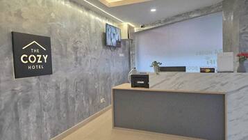 A reception desk with a modern design, a mounted television, and a sign indicating the name of the hotel.