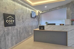 A reception desk with a modern design, a mounted television, and a sign indicating the name of the hotel. - The Cozy Hotel by Zuzu (Sungai Petani)