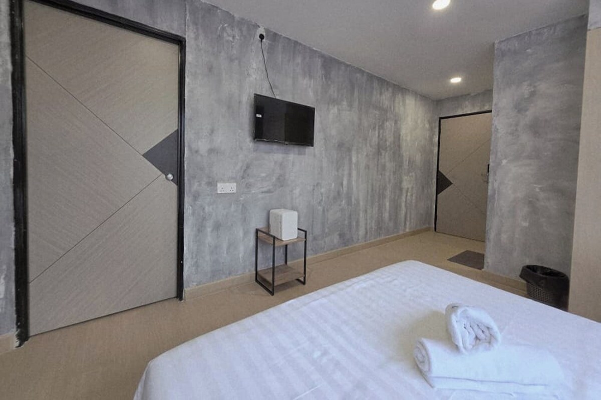 A modern hotel room with a large bed, a television mounted on the wall, and a small bedside table with a box.