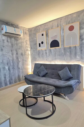 A modern living room with a grey sofa, a round glass table, and abstract wall art. - The Cozy Hotel by Zuzu (Sungai Petani)