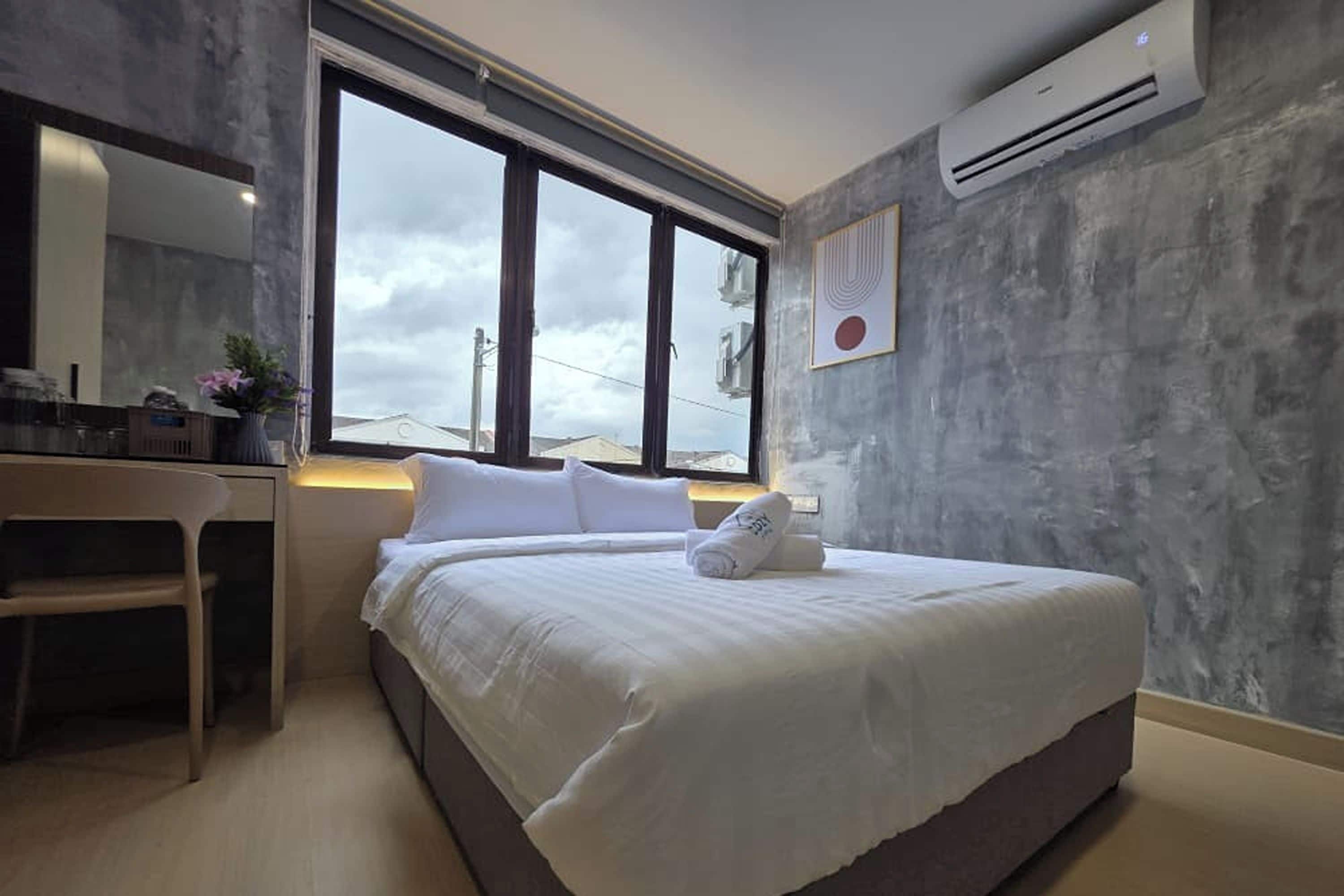 A modern hotel room with a large bed, a desk, and a window providing a view of the sky.