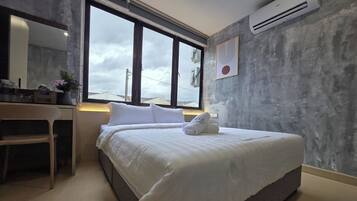 A modern hotel room with a large bed, a desk, and a window providing a view of the sky.