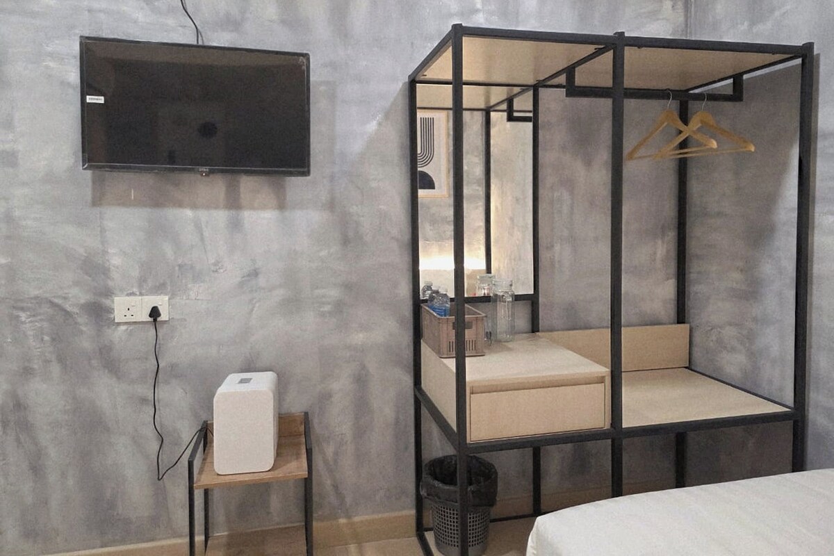 A modern room with a bed, a bedside table with a lamp, a TV mounted on the wall, and a hanging clothes rack.