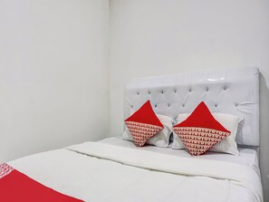 Una cama con cabecera blanca y dos almohadas rojas con un estampado repetido.