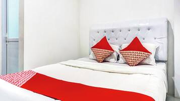 A bed with a white headboard, two red pillows, and a red throw blanket.