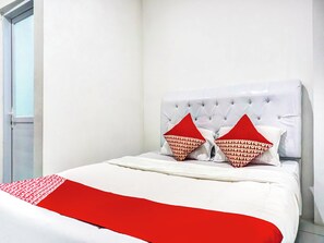 Uma cama com cabeceira branca, duas almofadas vermelhas e um cobertor vermelho.