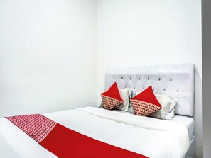 Cama com cabeceira branca e almofadas vermelhas, colcha branca e manta estampada em vermelho e branco.