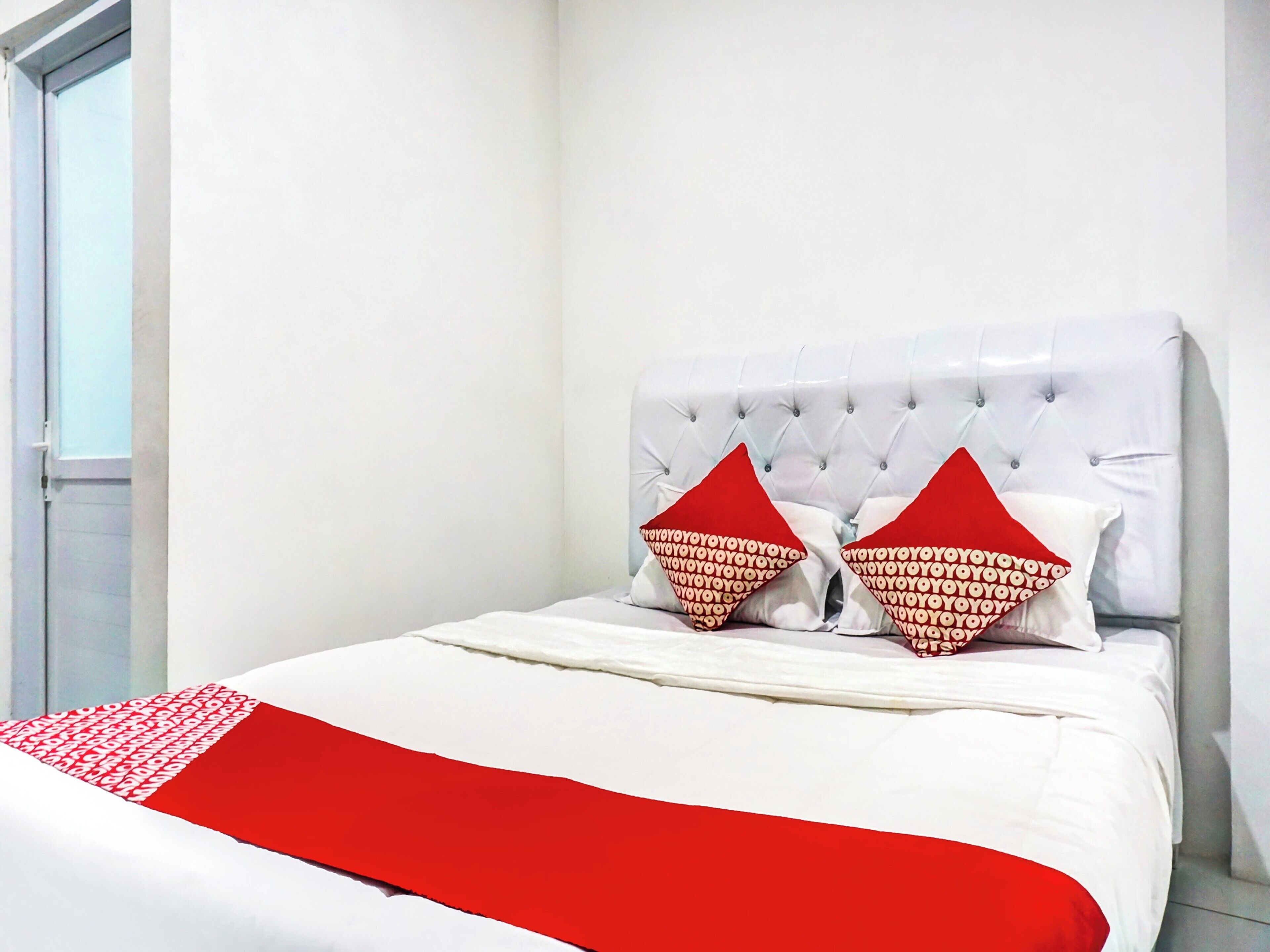 A bed with a white headboard, two red pillows, and a red throw blanket.