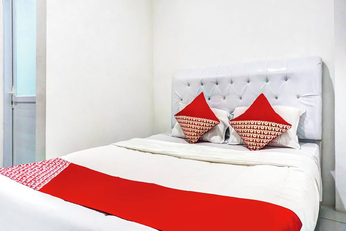 Uma cama com cabeceira branca, duas almofadas vermelhas e um cobertor vermelho.