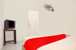 Una habitación con una cama, un televisor sobre un mueble, una puerta blanca y un ventilador fijado a la pared.