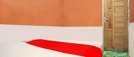 A bed with a white and red bedspread, a wooden door, and a patterned rug.