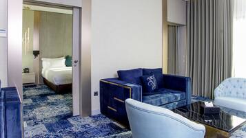 A hotel room with a bed, a blue sofa, a white armchair, and a coffee table.