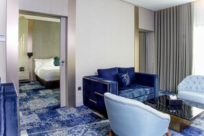 A hotel room with a bed, a blue sofa, a white armchair, and a coffee table. - Oriental Palace (Taza)