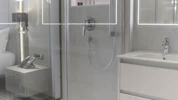 A modern bathroom with a glass-enclosed shower, a vanity with a mirror, and a bedside table with a lamp.