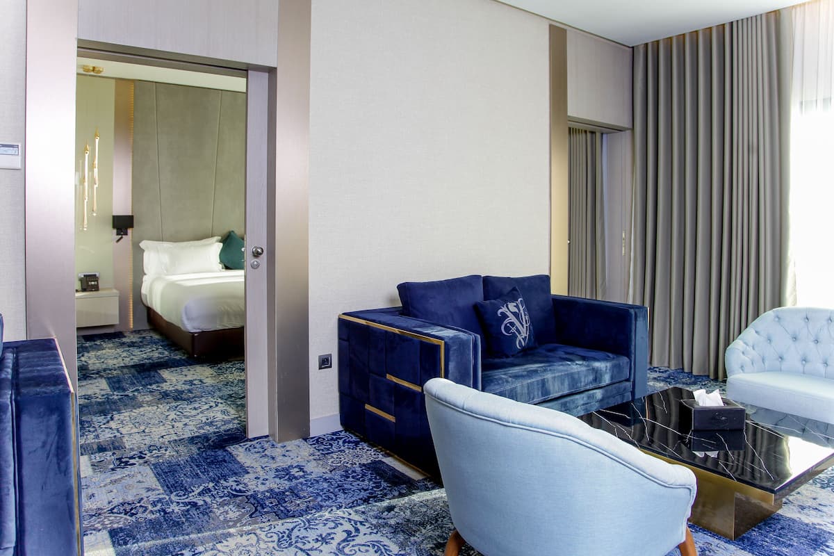 A hotel room with a bed, a blue sofa, a white armchair, and a coffee table.