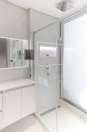 Une salle de bain moderne avec une douche à parois de verre, un meuble-lavabo avec un miroir et un téléviseur fixé au mur.