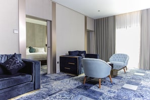 A hotel room with a dark blue sofa, a light blue armchair, a small table, and a patterned carpet.