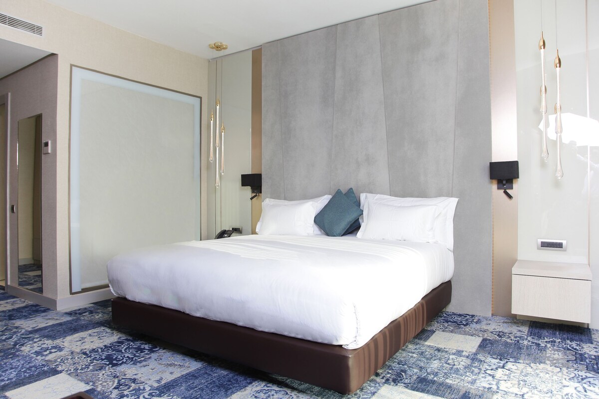 A hotel room with a large bed, a wardrobe, a bedside table, and a nightstand.