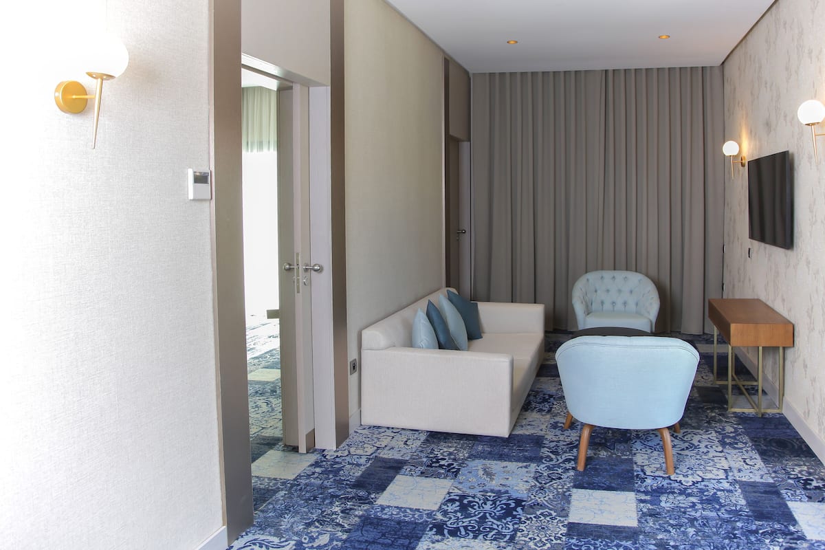 A hotel room with a sofa, armchair, and a television on the wall.