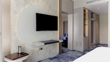 Une chambre d’hôtel moderne équipée d’un téléviseur à écran plat fixé au mur, d’une petite table de chevet et d’un dressing.