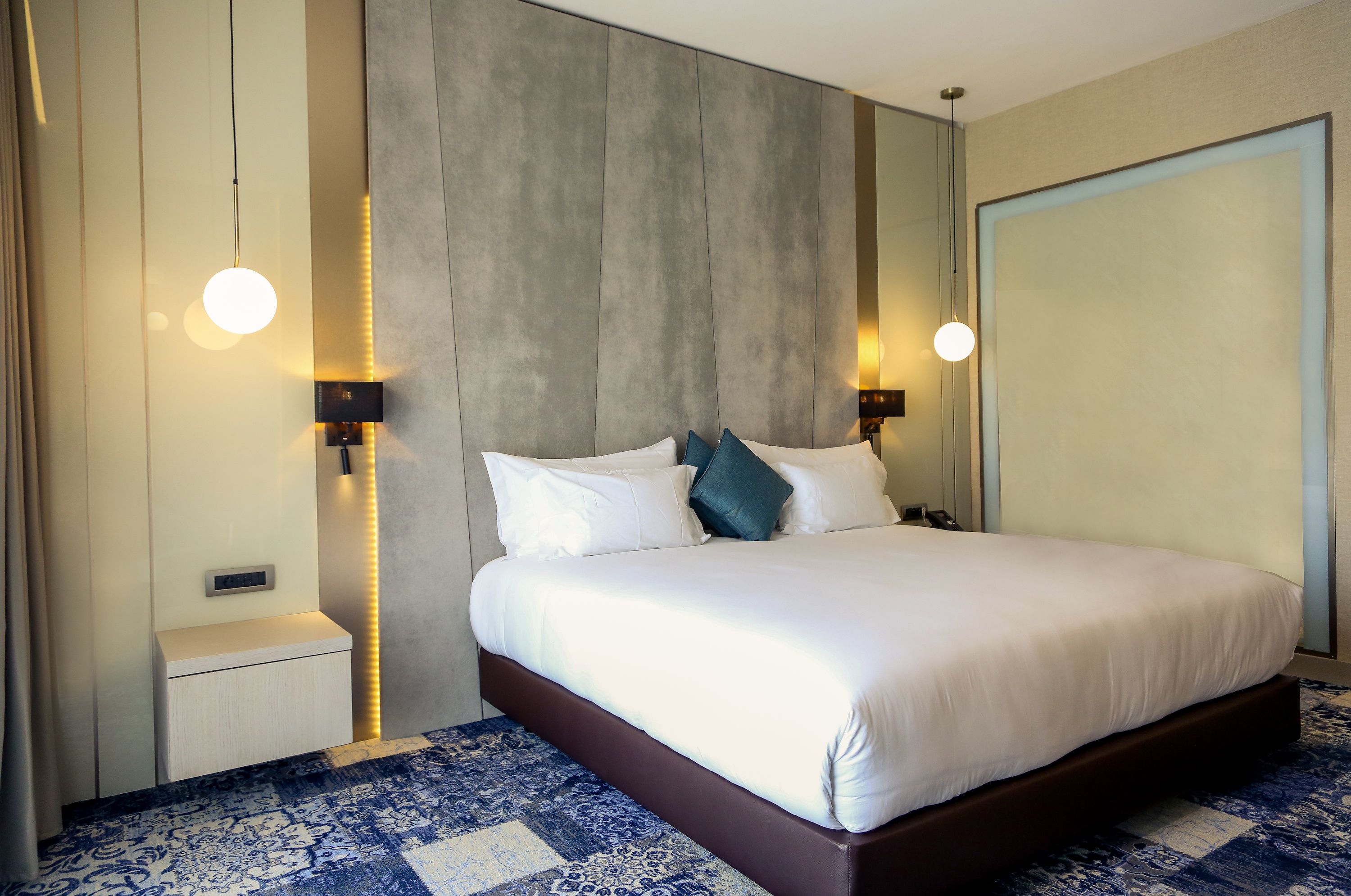 Ett modernt hotellrum med en stor säng, sänglampor, ett nattduksbord och en mönstrad matta.