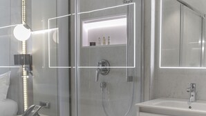 Un baño moderno con ducha envuelta en vidrio, un tocador con espejo y una mesita de noche con lámpara.