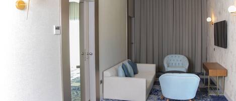 Una habitación de hotel con sofá, sillón y televisor en la pared.