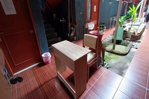 A wooden table and chair in a room with a tiled floor, a red door, and a small garden area with potted plants. - OYO 91341 D'phoenix Anggrek Syariah Residence (Jakarta)