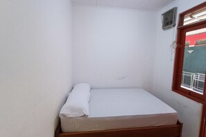 A small, single-bed room with a wooden bed frame, white bedding, a window with a metal railing, and a wall-mounted air conditioning unit. - OYO 91341 D'phoenix Anggrek Syariah Residence (Jakarta)