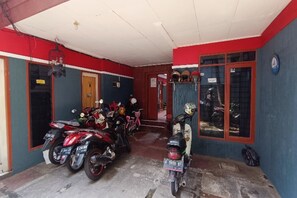 A motorcycle parking area with several motorcycles parked, a wooden door, and a blue wall. - OYO 91341 D'phoenix Anggrek Syariah Residence (Jakarta)