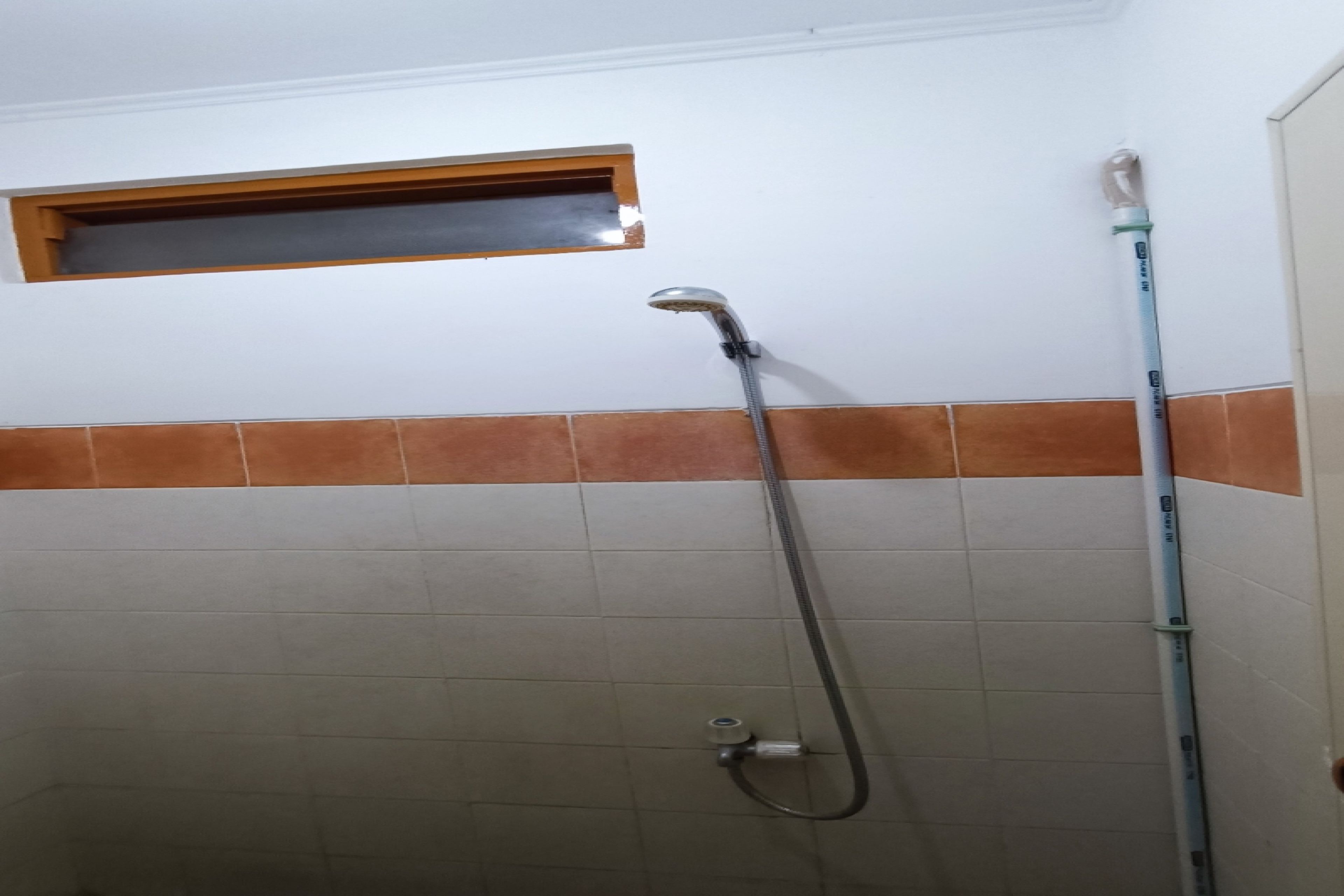 Une douche équipée d’un pommeau de douche à main, une fenêtre située au-dessus et un mur carrelé avec une bordure marron.