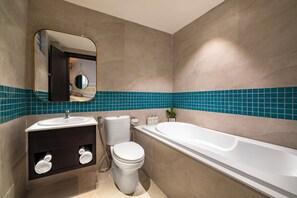 Ein modernes Badezimmer mit Waschbecken in Weiß, dunklem Waschtisch, Toilette und Badewanne.