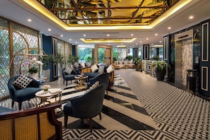 Eine moderne Hotelhalle mit einem geometrischen Fußbodenmuster, dunklen Sofas mit gemusterten Kissen und einer einzigartigen Deckenkonstruktion.