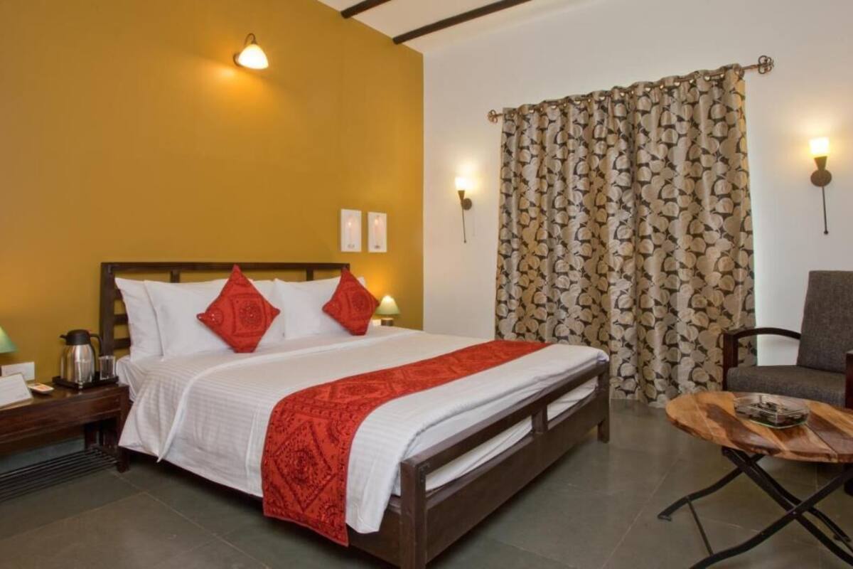 Una habitación de hotel con cama, mesita de noche, lámpara, silla y una mesa de madera.