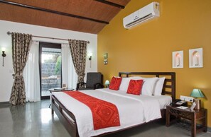 A hotel room with a bed, a chair, an air conditioning unit, a lamp, and a window with curtains. - Club Mahindra Gir (Mendarda)