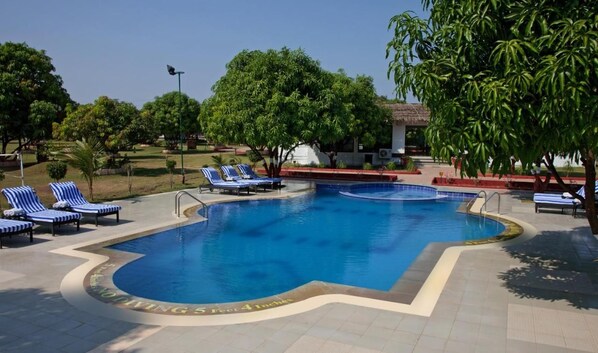 A swimming pool with blue water, surrounded by lounge chairs and trees. - Club Mahindra Gir (Mendarda)