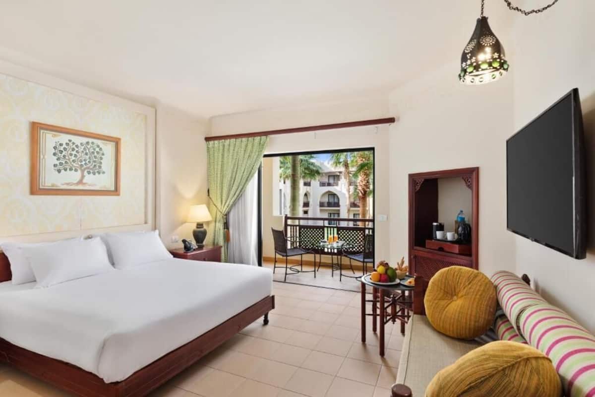 Een hotelkamer met een bed, een televisie, een zithoek met een tafel en stoelen, en een balkon met uitzicht.