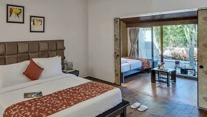 A hotel room with a large bed, a bedside table, a nightstand, a window with a view, and a door leading to an outdoor area. - Club Mahindra Saj Mahabaleshwar (Mahabaleshwar)