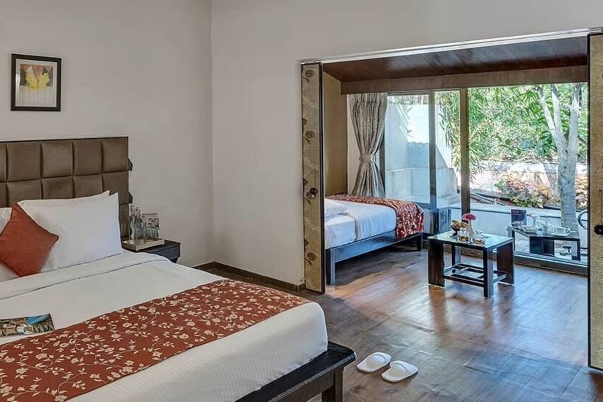 Une chambre d’hôtel dotée d’un grand lit, d’une table de chevet, d’une commode, d’une fenêtre offrant une vue agréable et d’une porte donnant sur un espace extérieur.