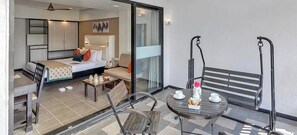 Een hotelkamer met een bed, een bank, een eettafel en een balkon met een bankje.