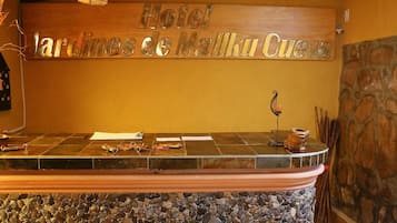 Una recepción con mostrador de piedra, una señal de madera encima y una pared de piedra a la derecha.