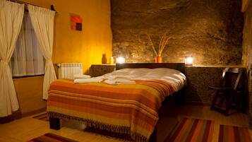 Un dormitorio con pared de piedra, cama con manta a rayas, suelo de madera y ventana con cortinas.