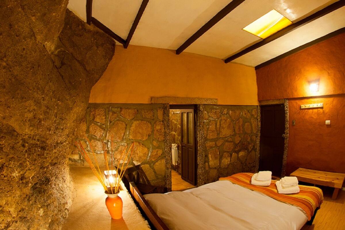 Un dormitorio con pared de piedra, una cama con toallas, un banco de madera y una pequeña mesa con una vela.