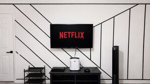 Ett modernt vardagsrum med en platt-TV som är monterad på väggen, en svart möbel för underhållningsutrustning placerad under TV:n och en fristående värmare till höger.