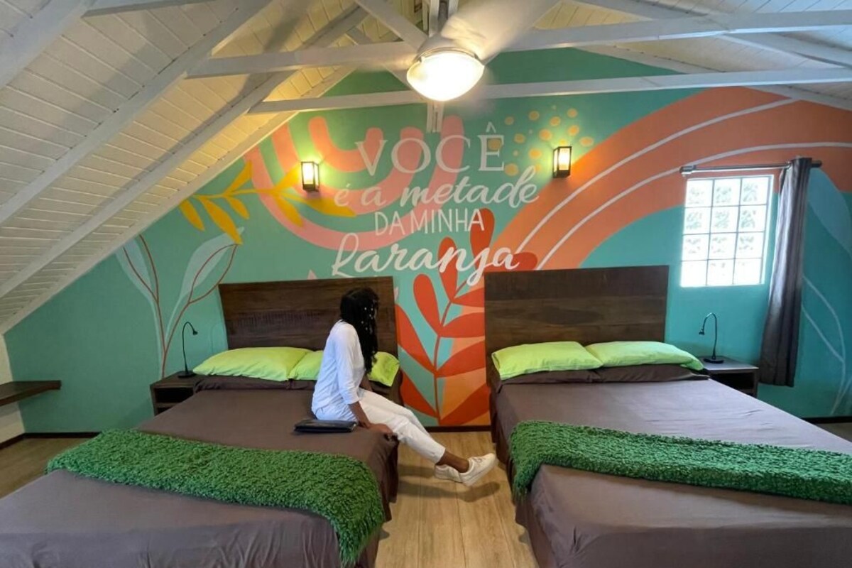 Une chambre avec deux lits, une fresque murale avec du texte, un ventilateur de plafond et une fenêtre avec des rideaux.